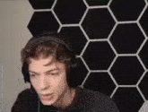 a young man wearing headphones is making a funny face in front of a black and white hexagon wall .
