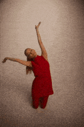 a woman in a red dress is kneeling down with her arms in the air