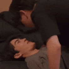 a man is kissing another man on the forehead while they are laying on a bed .