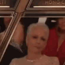 a woman in a white dress is sitting in a crowd of people applauding at an awards ceremony .