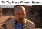a bald man with glasses and a beard is standing in the desert and making a funny face .