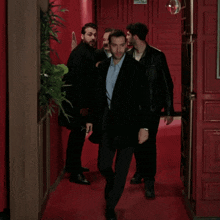 a group of men are walking down a hallway with a red door behind them