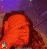 a man with long hair is covering his face with his hands .