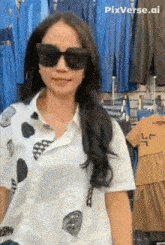 a woman wearing sunglasses and a white shirt stands in front of a display of clothes
