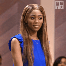 a woman in a blue top is standing in front of a be icon