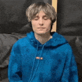 a young man with blonde hair is wearing a blue hoodie .