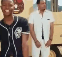 a couple of men are standing next to each other in a room . one of the men is wearing a baseball jersey .