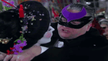 a man in a purple mask kisses a woman in a white mask