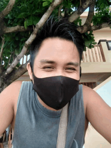a man wearing a black face mask and a grey tank top smiles