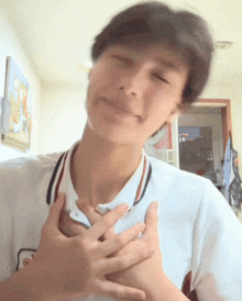 a man in a white shirt has his hands on his chest and his eyes are closed