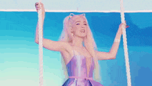a woman in a purple dress is hanging from a rope on a swing .