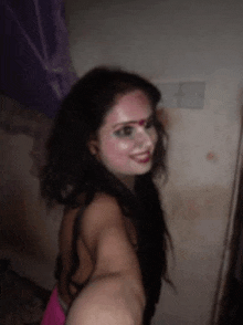 a woman in a pink dress is taking a selfie with her face painted .