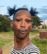 a man with pigtails on his head is standing in a field and making a funny face .