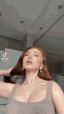 a woman with red hair is wearing a tank top and earrings and holding her hair .