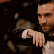 a man in a tuxedo with a bow tie holds his hand to his chin