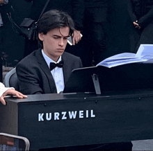 a man in a suit and bow tie is playing a keyboard that says kurzweil