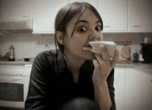 a woman is eating a sandwich in a kitchen and making a funny face