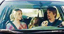 a man is driving a car with a woman and a child in the back seat .