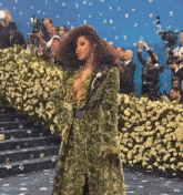 a woman in a green coat stands in front of a crowd of people taking pictures