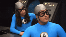 two men in blue superhero costumes with the letter a on them