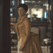 a woman in a gold dress is standing in a room with hbo written on the bottom