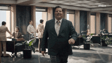 a man in a suit and tie walks through an office with the word max on the bottom right