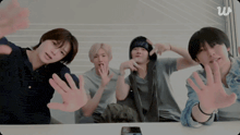a group of young men are sitting at a table with their hands up in front of a screen that says w on it