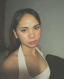 a young woman in a white tank top looks at the camera