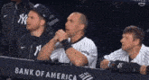a group of baseball players are sitting in a dugout with a bank of america banner behind them