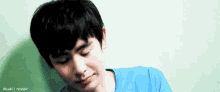 a young man in a blue shirt is making a funny face against a green wall .