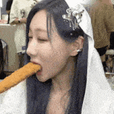 a woman wearing a white veil is eating a fried food stick