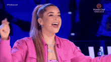 a woman in a pink jacket is laughing in front of a microphone and a masterchef logo