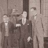three men in suits and bow ties are standing in a room