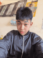 a young boy in a black jacket takes a selfie in front of a wall with pictures on it