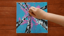a person is painting a tree with pink flowers on a blue background