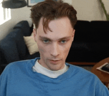 a man in a blue shirt is looking at the camera with a couch in the background