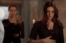two women are standing next to each other in a room . one of the women is holding another woman 's hand .