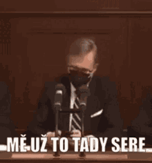 a man in a suit and tie is wearing a mask and speaking into a microphone .