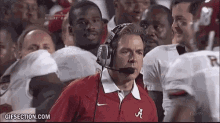 a man wearing headphones and a red shirt with the letter a on it stands in front of a group of football players .