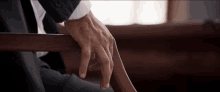 a man in a suit and tie rests his hand on the arm of a wooden chair