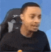 a man in a black shirt is sitting in a chair and making a face .