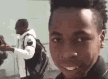 a young boy with a backpack is smiling at the camera while another man stands behind him .