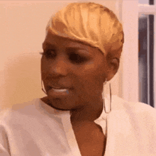 a woman with short blonde hair is wearing a white shirt and earrings and making a funny face .