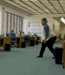 a man in a baseball cap is walking in a room with a lot of chairs