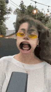 a woman wearing yellow sunglasses and a white shirt has her mouth wide open