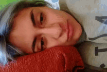 a woman with blue hair is laying on a pillow with the letter t on her shirt .