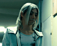 a man with long blonde hair is wearing a white jacket and a t-shirt that says nothing on it