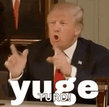 a man in a suit and tie is sitting at a table making a funny face and pointing at the camera .