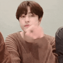 a young man wearing a brown sweater is making a funny face .
