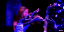 a crowd of people are dancing in a dark room with purple lights .